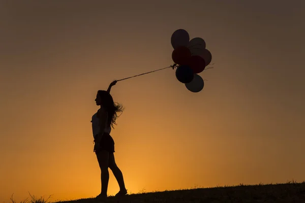 Jovem mulher com balões ao pôr do sol — Fotografia de Stock