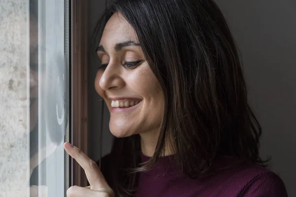 Jeune femme souriant par la fenêtre — Photo
