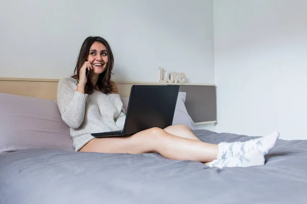 Wanita muda duduk di tempat tidur menggunakan laptop — Stok Foto