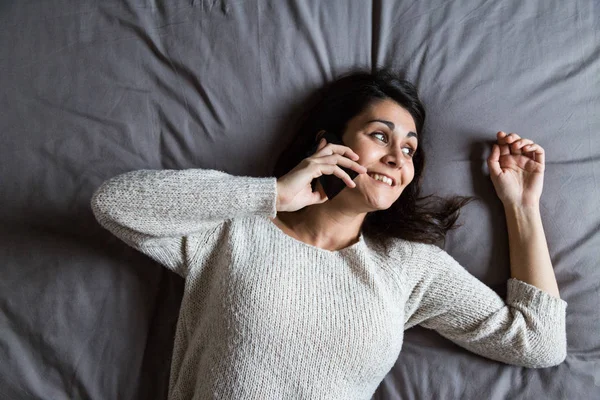 Wanita muda berbicara di telepon di tempat tidur — Stok Foto