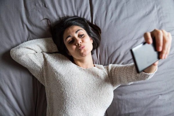 Wanita muda mengambil selfie di tempat tidur — Stok Foto