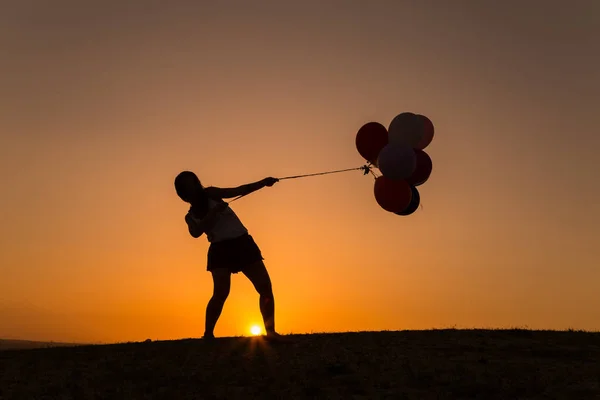 Günbatımında balonlarla oynayan genç bir kadın silüeti — Stok fotoğraf