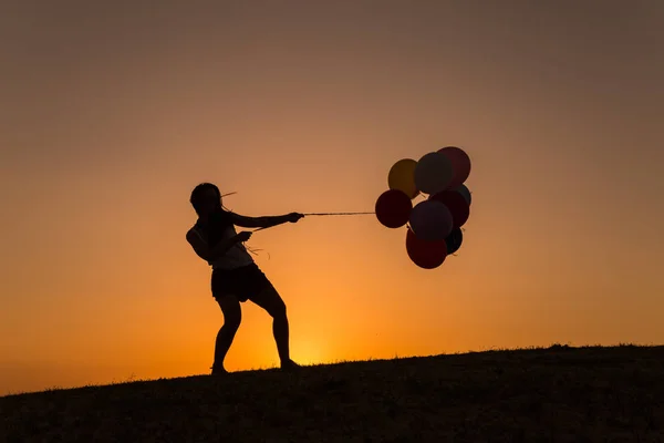 Silhueta de uma jovem mulher brincando com balões ao pôr do sol — Fotografia de Stock