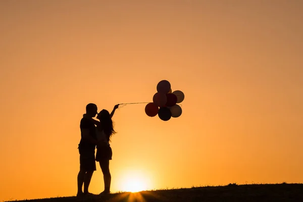 Silhueta de um casal brincando com balões ao pôr do sol — Fotografia de Stock