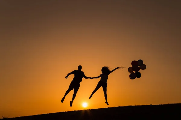 Silhueta de um casal brincando com balões ao pôr do sol — Fotografia de Stock