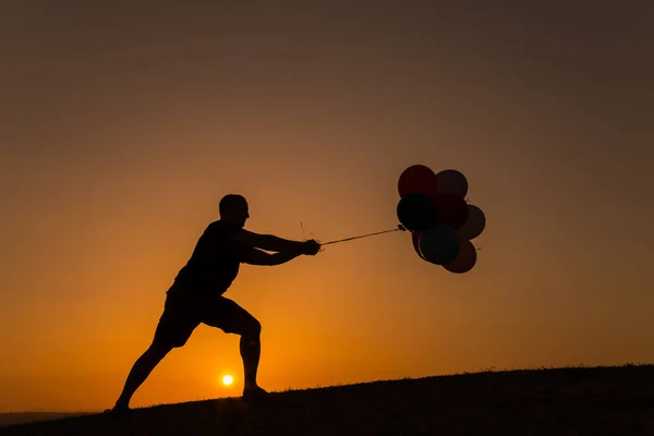 Силует чоловіка, який грає з повітряними кулями на заході сонця — стокове фото