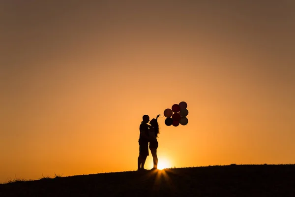 Silhueta de um casal brincando com balões ao pôr do sol — Fotografia de Stock