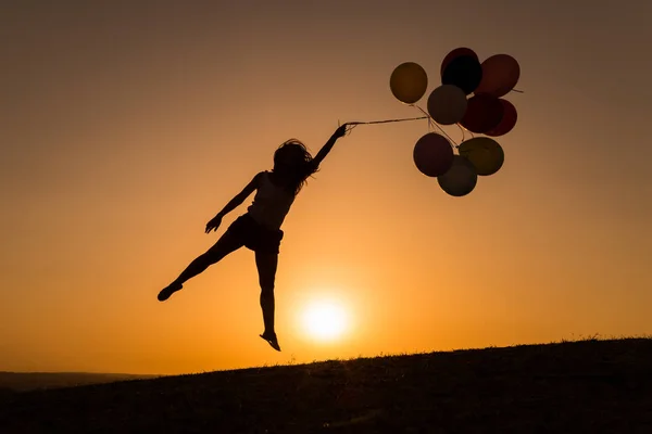 Sziluettjét, egy fiatal nő játszik léggömbökkel a naplemente — Stock Fotó