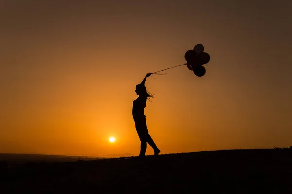 Siluet seorang wanita muda bermain dengan balon saat matahari terbenam — Stok Foto