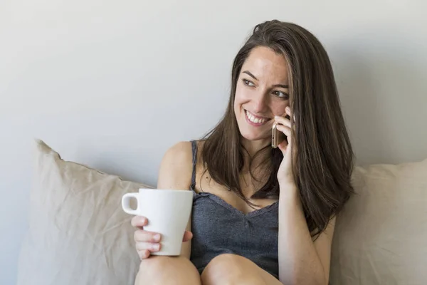 Wanita muda yang cantik menikmati kopi di tempat tidur dan berbicara di — Stok Foto
