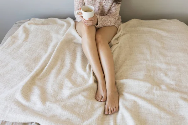 Ung kvinna njuter av hennes kaffe medan du sitter i sängen. Ovanifrån. — Stockfoto