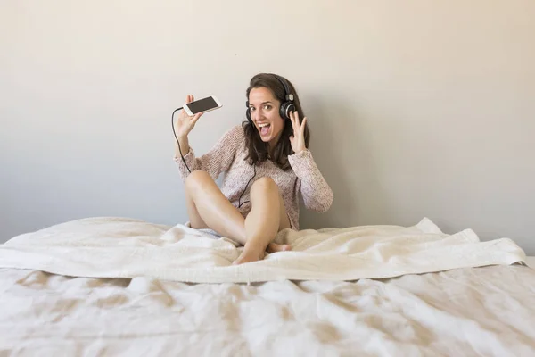 Happy young woman listening to music on bed with mobile phone an — Stock Photo, Image