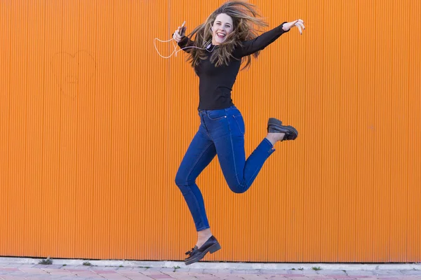 Wanita muda yang cantik mendengarkan musik dengan earphone dan melompat — Stok Foto