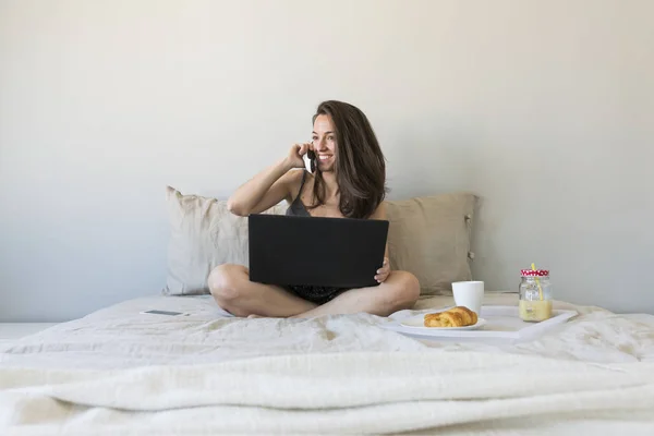 Piękna młoda kobieta siedzi na łóżku za pomocą laptopa i ciesząc się h — Zdjęcie stockowe