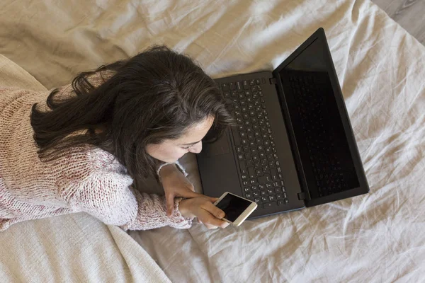 Piękna młoda kobieta leżąc na łóżku, za pomocą laptopa. Kawa na rękę — Zdjęcie stockowe