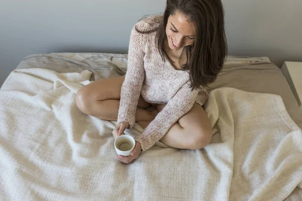 Kvinna som håller en kopp kaffe i hennes sovrum. sitter på sängen och — Stockfoto