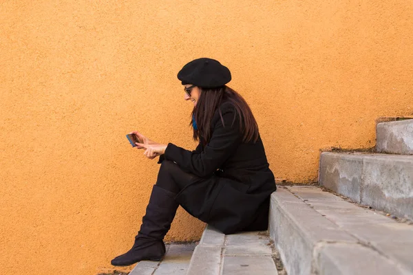 Wanita muda yang cantik bahagia menggunakan ponsel pintarnya melalui orange ba — Stok Foto