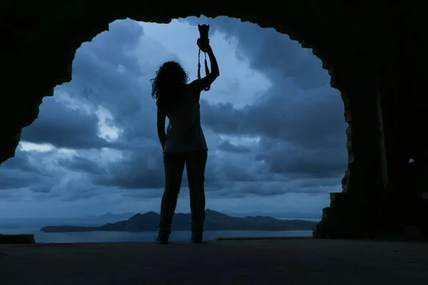 S tarafından kaya üzerinde bir kamera tutan bir youn kadın silüeti — Stok fotoğraf