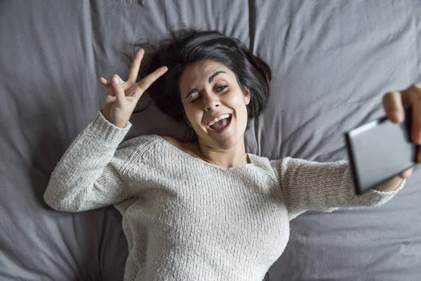 Piękna młoda kobieta, biorąc selfie z inteligentny telefon na łóżko — Zdjęcie stockowe