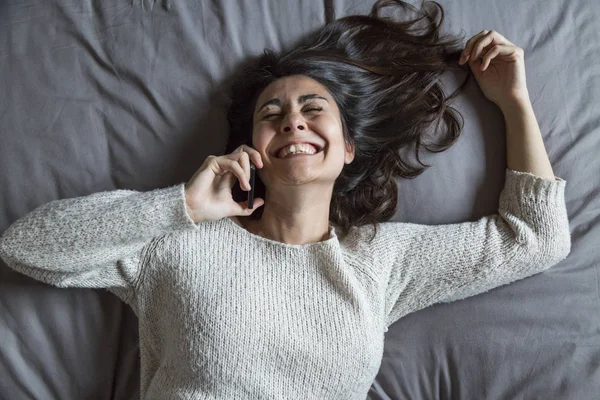 Szczęśliwy piękna dziewczyna leżąc na łóżku i rozmawia przez telefon ona i — Zdjęcie stockowe
