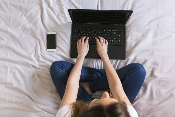 Wanita muda bekerja pada laptop di rumah di tempat tidur. Lihat dari atas — Stok Foto