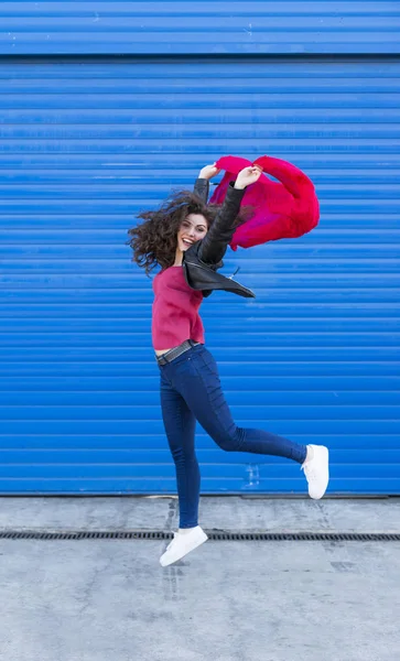 Giovane donna che salta e si diverte con una sciarpa rossa sopra b blu Immagini Stock Royalty Free