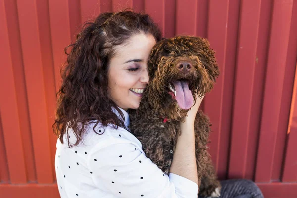 Wanita muda yang cantik memeluk anjingnya, anjing air Spanyol berwarna coklat — Stok Foto
