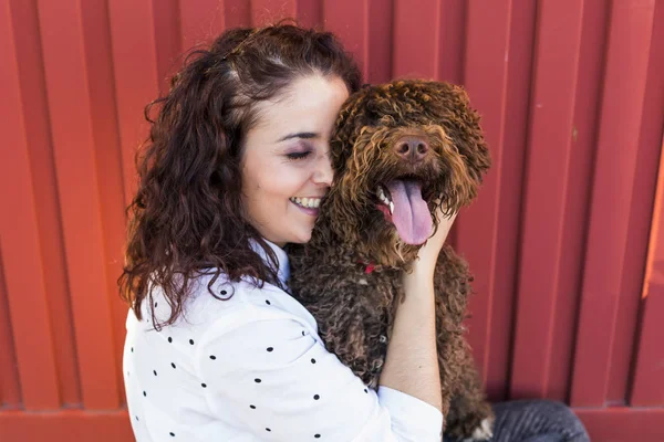 Güzel genç kadın köpeğini, kahverengi bir İspanyol su köpeği sarılma