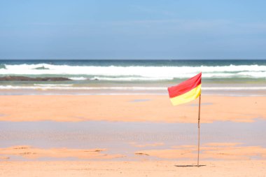 Okyanusun önünde kırmızı sarı bir bayrak dalgalanıyor. Uyarı, mesaj.