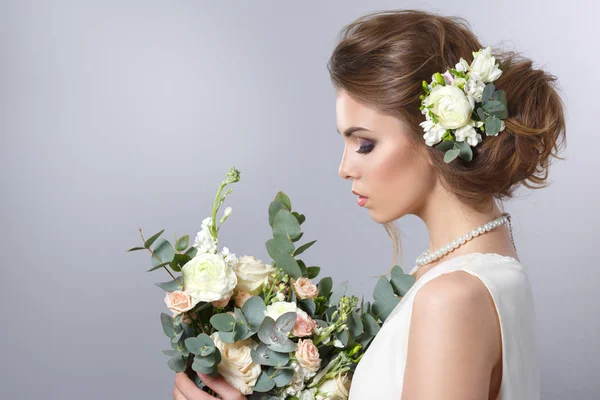 portrait of bride hairstyle with wreath and bouquet in hands on gray background