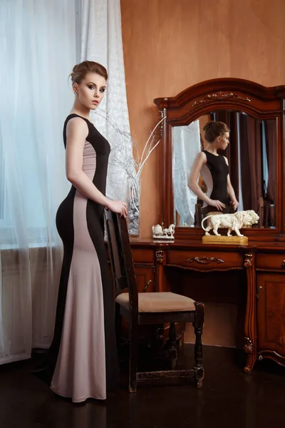 修长的女孩穿着长裙站立在豪华古典内饰镜子附近 — 图库照片