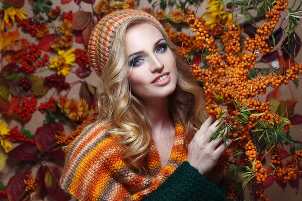 Autumn portrait of a beautiful woman in a scarf and a hat on a background of panels of leaves and berries