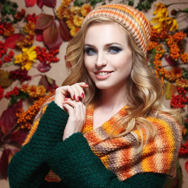 Autumn portrait of a beautiful woman in a scarf and a hat on a background of panels of leaves and berries