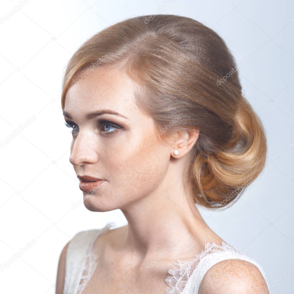 Beauty portrait of a red-haired bride with freckles and a beautiful hairstyle on gray background.