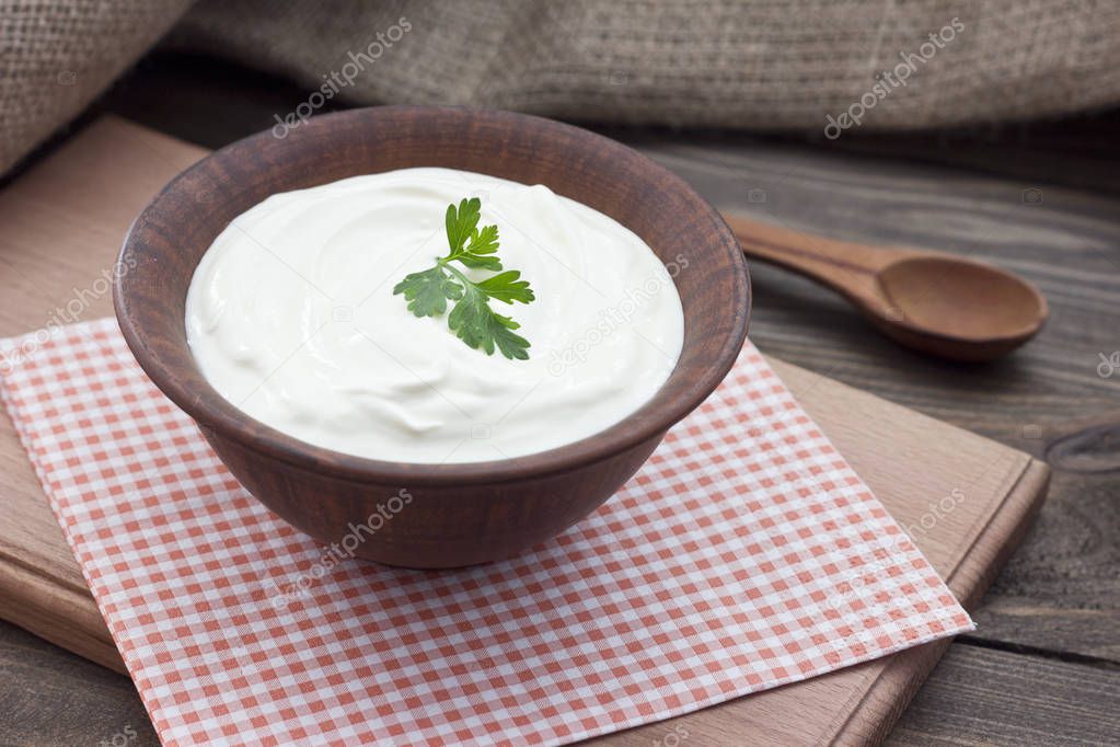 sour cream in a clay bowl on a table with fresh herbs