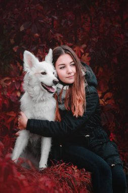 Güzel genç kız beyaz köpeği nehir kıyısında sonbahar sabahı sarılma.