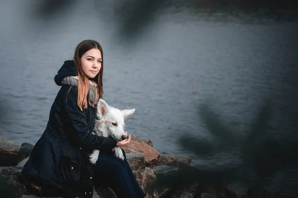 Beautiful teenager girl hugging her white dog on the bank of the river autumn morning — Stock Photo, Image
