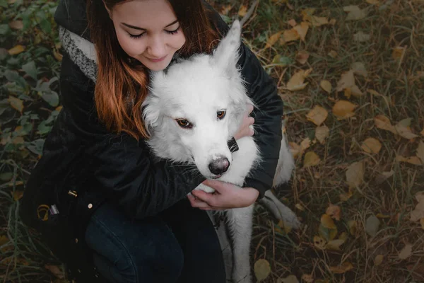 Beautiful teenager girl hugging her white dog on the bank of the river autumn morning — Stock Photo, Image