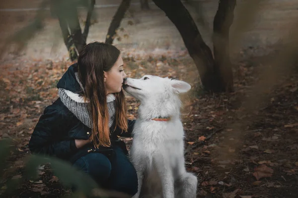 Beautiful teenager girl hugging her white dog on the bank of the river autumn morning — Stock Photo, Image