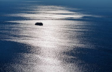 Güçlü güneş ışığıyla denizde giden bir geminin silueti.