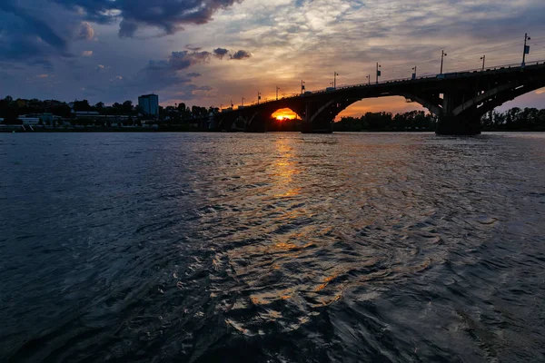 Günbatımında dalgalar, güneş ve bulutlarla Angara nehri üzerinde eski bir köprü. — Stok fotoğraf