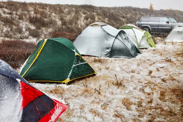 Camping with colorful tents in snow storm in autumn