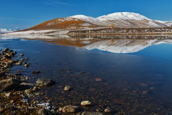 Horské jezero v září s tenkým ledem a odrazem kopce za slunečného dne — Stock fotografie