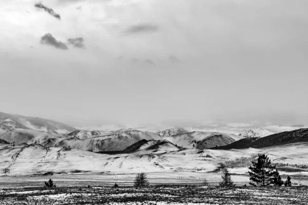 Skalnaté kopce pokryté sněhem v oblačném počasí v černobílé sněhové bouři — Stock fotografie