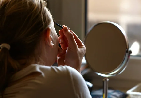 Gadis muda melakukan make up di rumah di depan cermin bulat Stok Lukisan  