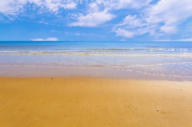 Mavi gökyüzünün ve beyaz bulutların altındaki deniz ve sahil.