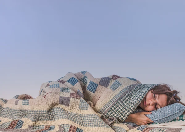 Jeune femme dormant sous une couverture à carreaux — Photo