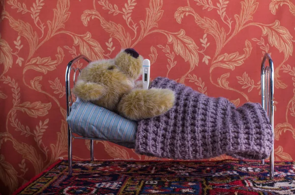 Больной одинокий плюшевый мишка лежит с термометром в постели — стоковое фото