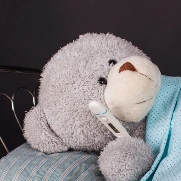 Sick teddy bear lying in bed with a temperature