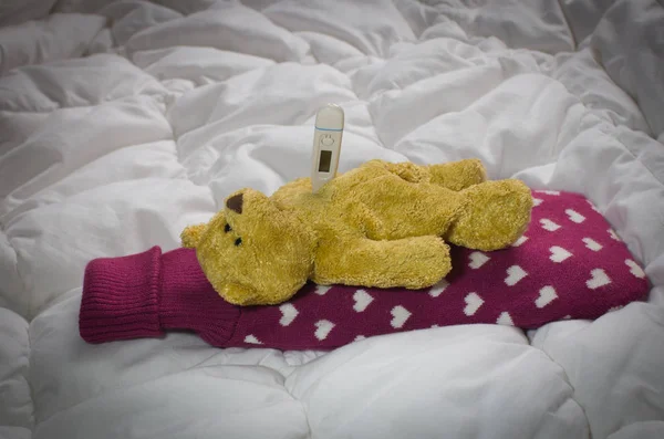 Sick teddy bear lying  with  hot-water bottle and thermometer